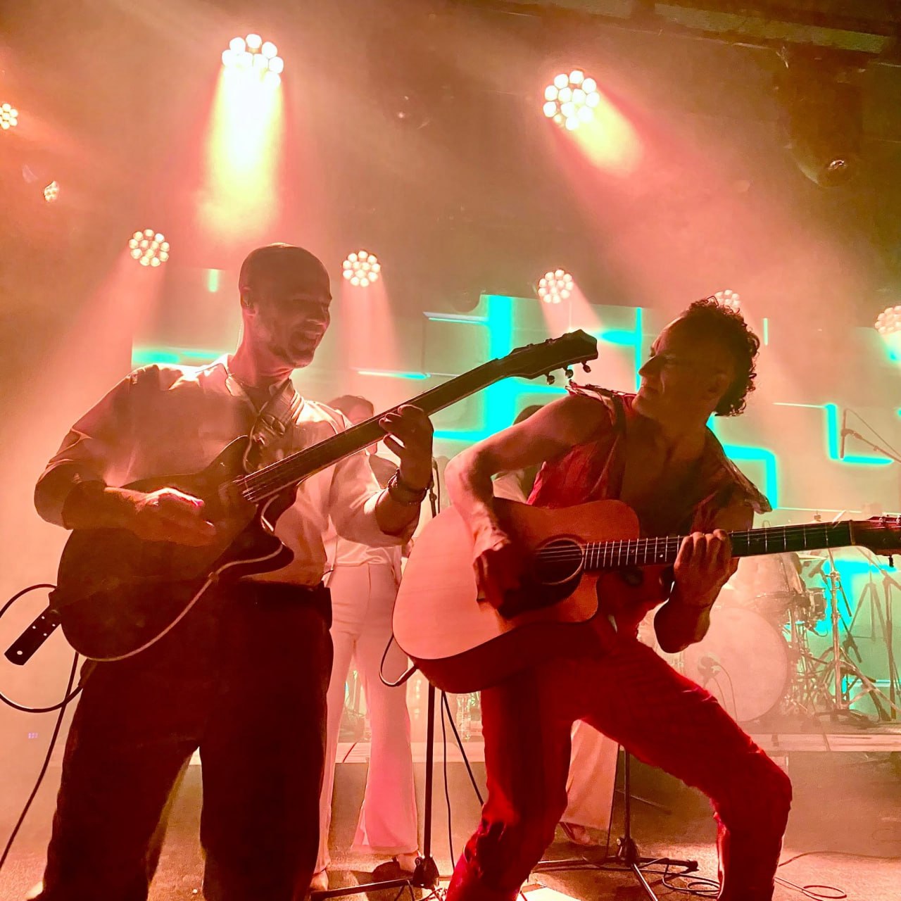 Olive Shows David Bowie tribute - two guitarists playing acoustic guitars side by side under warm and teal stage light
