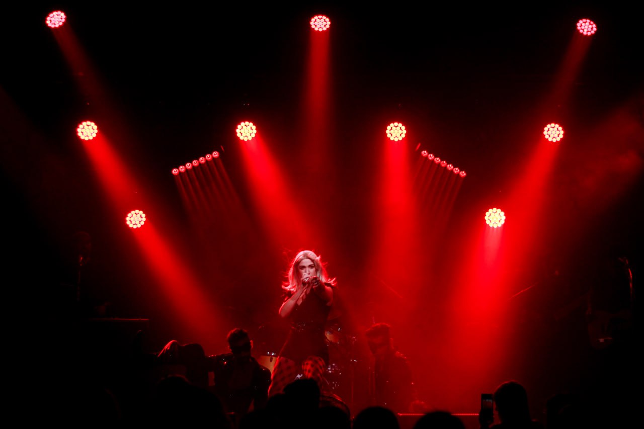 Olive Shows Madonna tribute - the soloist singing center stage beneath a fan of red spotlights above a filming crowd