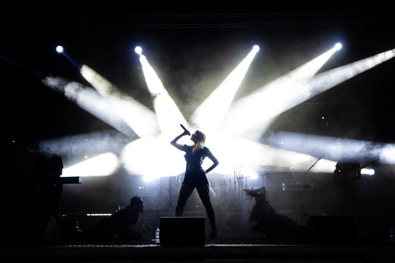 Olive Shows Madonna tribute - silhouette of the soloist with a hand on her hip against a starburst of white spotlights