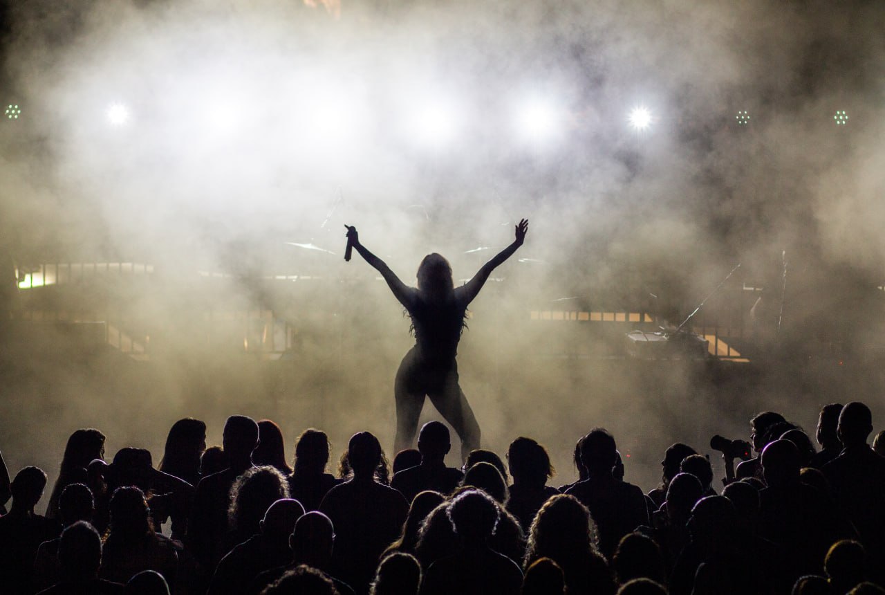 Olive Shows Madonna tribute - silhouette of the soloist from behind with both arms spread wide in the haze above the crowd